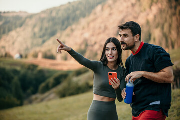 Active duo taking a break on a hilltop trail, enjoying water and mobile technology after jogging