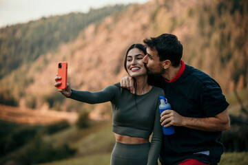 Multicultural pair in workout attire taking a breather, staying hydrated, and using smartphone for a selfie