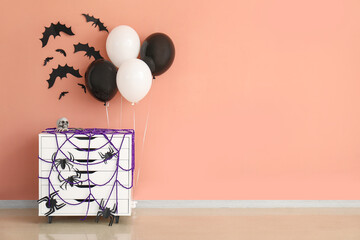 Stylish chest of drawers, balloons and Halloween decor near color wall in room