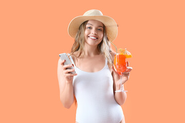 Beautiful young woman in swimsuit with glass of tasty aperol spritz and mobile phone on orange...