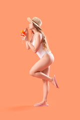 Beautiful young woman in swimsuit drinking tasty aperol spritz on orange background