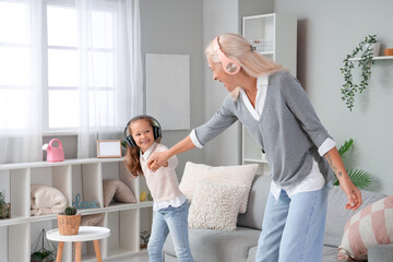 Fototapeta premium Little girl with her grandmother in headphones dancing at home
