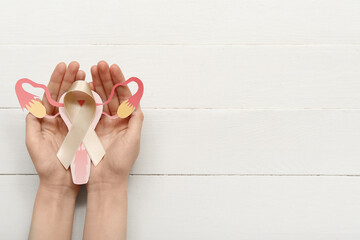 Woman with beige ribbon and paper uterus on white wooden background. Cancer awareness concept