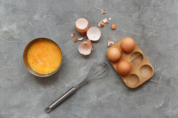 Bowl with beaten chicken eggs and whisk on grey background