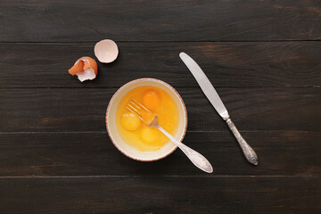 Bowl with cracked chicken eggs on wooden background