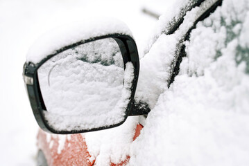 Right side mirror of a parked car. Snow covered car mirror closeup, selective focus. Snowy vehicle on parking lot in winter day.