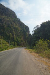 Fototapeta premium The route of the damaged road is mixed with a dirt road with views of forests and mountains on both sides.