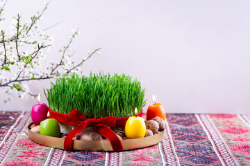 Beautiful Novruz tray on rug with semeni - wheat grass with red ribbon, festive candles on national...