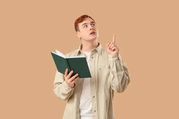 Young man holding book and pointing at something on color background