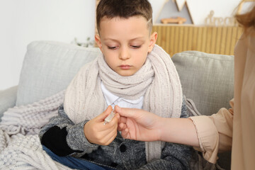 Ill little boy with thermometer and his mother at home