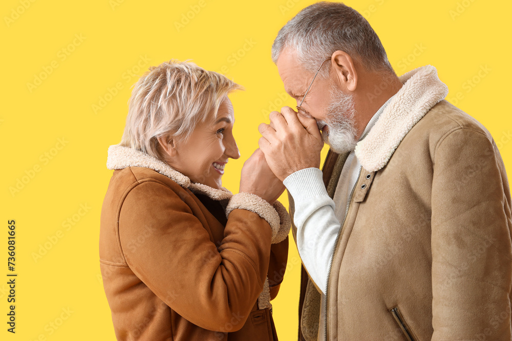 Poster Mature couple in sheepskin coats warming hands on yellow background