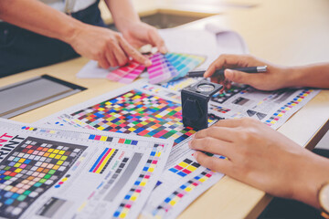 Crop image of worker checking print quality of media graphics proof print and color tone in...