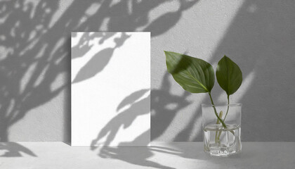 vertical sheets of textured white paper against a soft gray table background. the natural light creates subtle shadows from an exotic plant, enhancing the mockup overlay in a horizontal