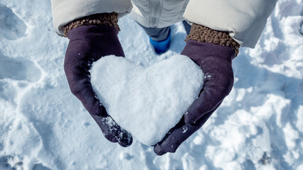 Female hands in knitted mittens with snowy heart against snow background stock photo - 736086847