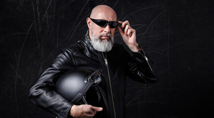 Portrait d'un motard homme avec un casque noir et une veste en cuir et des lunettes de protection et une barbe grise vintage