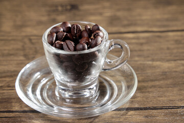Smoke vape fog flowing out of transparent glass coffee cup filled with coffee beans on dark black background