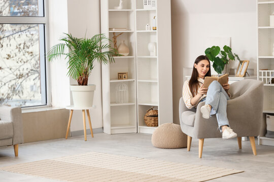 Beautiful woman reading book in armchair at home