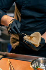 close-up of a chef in black gloves putting different sauces on bun with a spoon