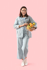 Young woman with basket of fruits on pink background