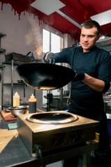 smiling chef in the kitchen holding and stirring noodles against the backdrop sunset