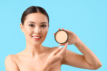 Obraz na płótnie Canvas Young Asian woman with makeup powder on blue background, closeup