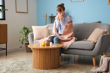 Ill young woman with tissue sneezing on sofa at home