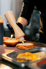 close-up on the table hands pour sauce from a bottle onto bun an almost finished burger