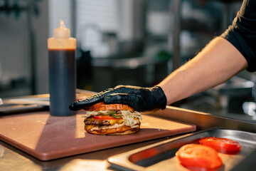 close-up of the hands of a chef in the kitchen of a restaurant attaching one half of a bun to the...