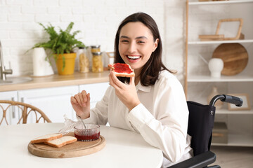 Happy young woman in wheelchair eating toast at home