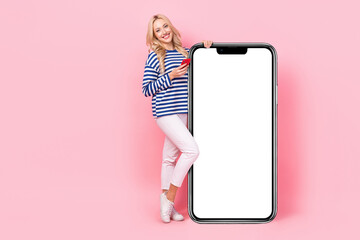 Full length photo of pretty funny woman dressed striped shirt texting modern gadget empty space isolated pink color background