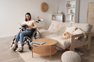 Happy young woman in wheelchair with Pomeranian dog reading magazine at home