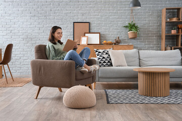 Happy young woman reading book in armchair at home