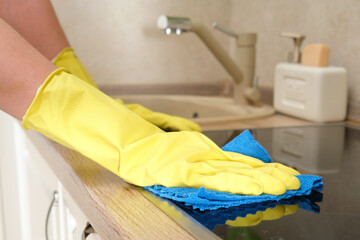 A woman washes an induction stove in her home kitchen with a blue cloth. Women's hands in yellow...