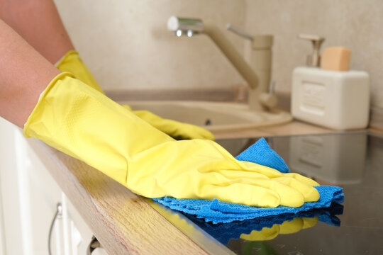 A woman washes an induction stove in her home kitchen with a blue cloth. Women's hands in yellow gloves while cleaning the kitchen
