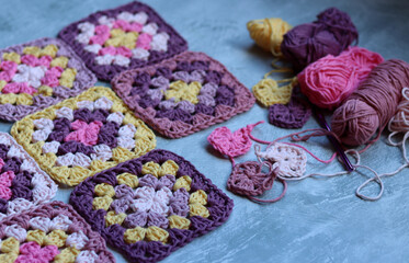 Granny squares crocheting in process. Colorful Afghan squares pattern close up photo. Grey background with copy space.  