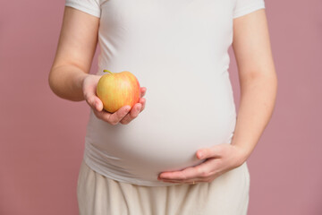 Pregnant woman holding apple fruit in her hand, studio pink background. Concept of pregnancy and proper nutrition