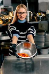 young girl with glasses in the kitchen stands and holds out a bowl of sweet potato demonstrating the product to the camera