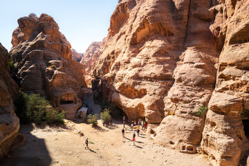 Unregognizable tourists walk in a desert valley surrounded by eroded sandstone hills on a hot sunny...