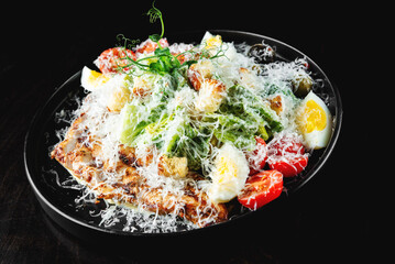 Caesar salad with croutons, cheese, eggs, tomatoes and grilled chicken on wooden table