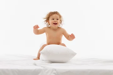Fotobehang Playful and funny little baby-girl playing, have fun on bed and jumping on soft pillow against white background. Concept of childhood and carefree, motherhood, life, birth. Copy space for ad © Lustre