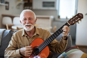 Obraz premium A lonely man with a beard enjoys playing the guitar at home. Senior man playing guitar at home.