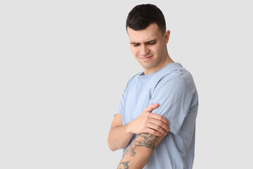 Young man suffering from arm pain on light background