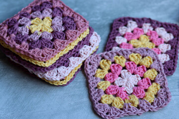 Handmade crocheted zigzag ornaments on grey background with copy space. Colorful cotton granny square. Crochet texture close up photo. 