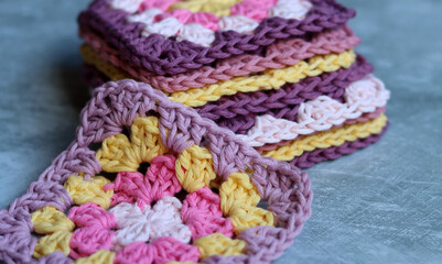 Handmade crocheted zigzag ornaments on grey background with copy space. Colorful cotton granny square. Crochet texture close up photo. 