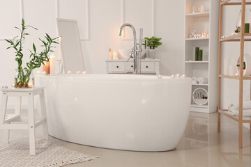 Interior of light bathroom with burning candles, bathtub and mirror