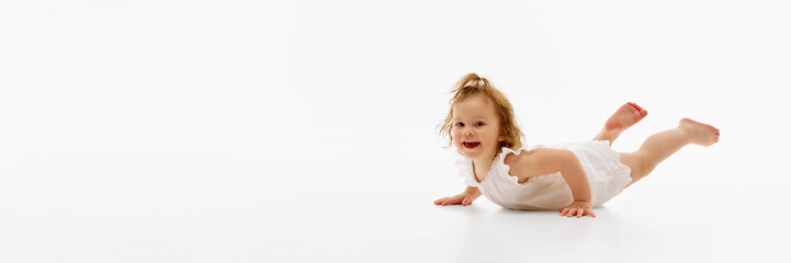 Banner. Carefree, cute smiling little baby, lying on floor in dress against white background with...
