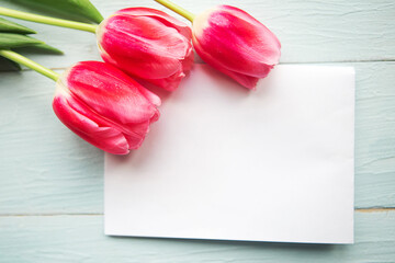 pink tulips and white mockup blank on wooden background. Flat lay, top view, copy space. Easter or Mother's Day greeting card