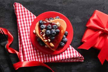 Plate with tasty pancakes in shape of heart, jam, blueberry and gift box on dark background. Valentine's Day celebration