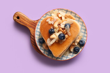 Plate with tasty pancakes in shape of heart, blueberry and nuts on purple background. Valentine's Day celebration
