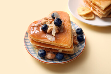 Plate with tasty pancakes in shape of heart, blueberry and nuts on beige background, closeup. Valentine's Day celebration